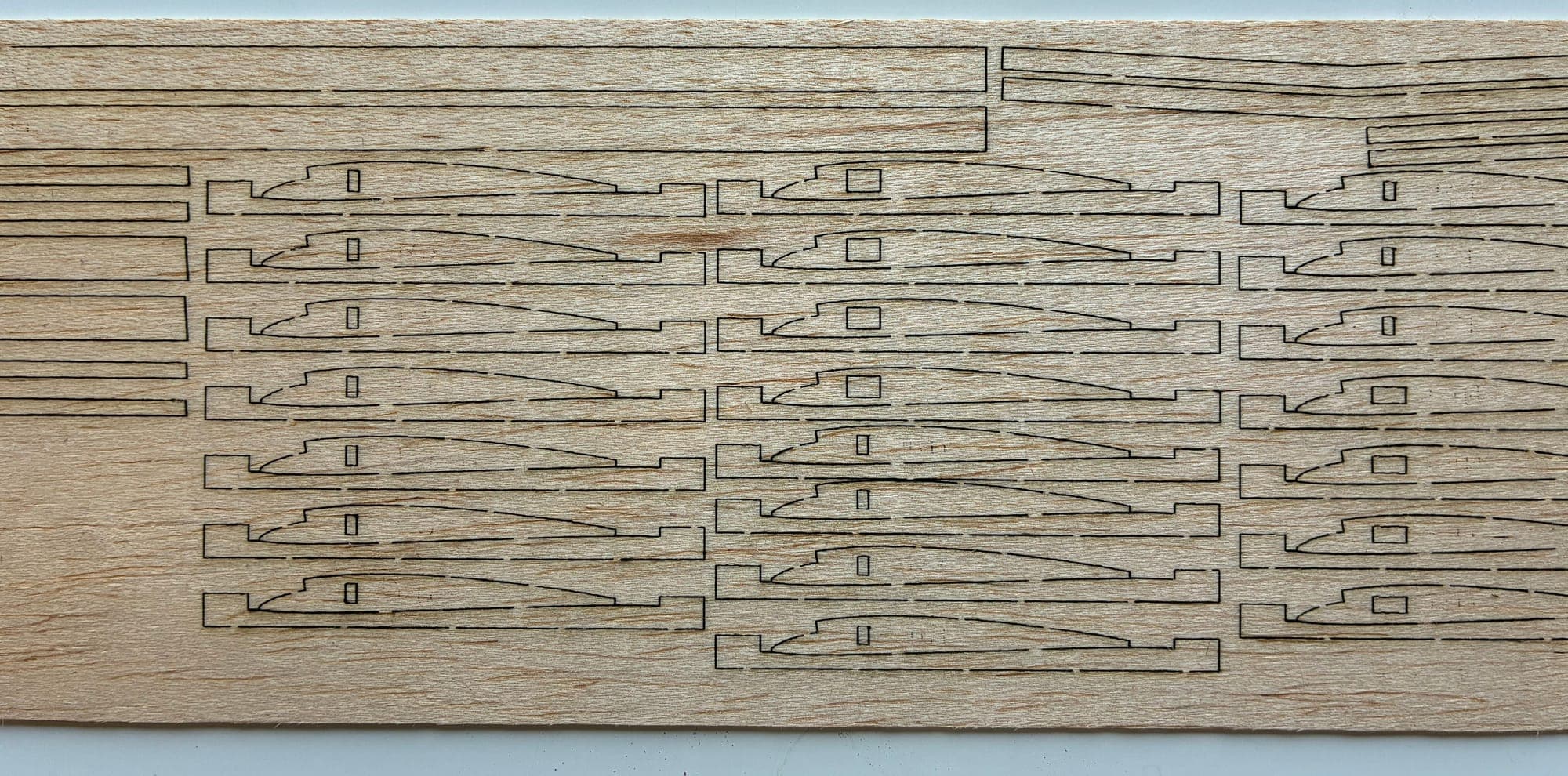 Laser-cut balsa sheet with rows of wing ribs nested and held by retention tabs